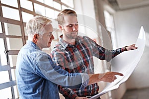 Is this where you want the window. two male architects discussing blueprints while standing indoors.