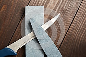 Whetstones and steel knife blade. Grindstones. Oval and rectangular double layer sharpening stone on wooden table background