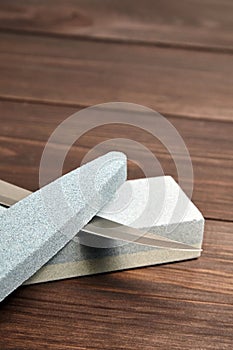 Whetstones and steel knife blade. Grindstones. Oval and rectangular double layer sharpening stone on wooden table background