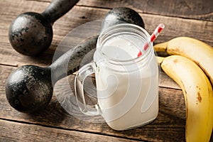 Whey protein cocktail, vintage dumbbells and banana fruit on wooden table