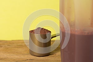 Whey Protein. Close up of scoop with chocolate powder and shaker