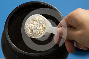 Whey Protein. Point of view of hand holding measuring scoop. Vanilla flavour. Color background: blue