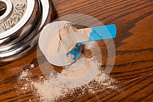 Whey protein powder in measuring scoop and dumbbell on wooden