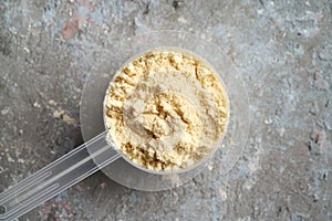 Whey protein powder in a measuring scoop on textured background