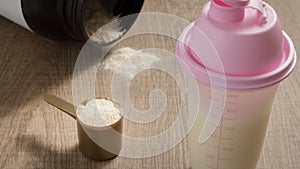 Whey Protein. Dropped black jar and spilled powder. Yellow measuring scoop. Selective focus and wooden table.