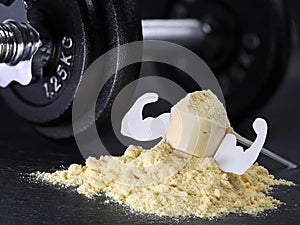 Whey protein scoop with mucles on powder heap with dumbbell on black background, muscle gain from protein shakes