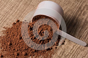 Whey Protein. White scoop on wooden background with chocolate po