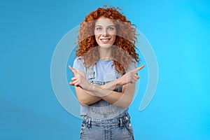 Which way. Charismatic attractive happy smiling redhead curly girl pointing curious sideways cross arms body indicating