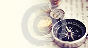 Which way to the big payout. Studio shot of coins and a compass on the business section of a newspaper.