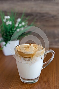 Whipped Coffee or Dalgona Coffee with creamy soft peak on a table with brown tone and decorated plant in the background