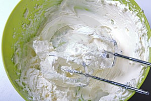 Whipped cream in a container. In it lie the corollas of the blender. Cream for decorating the cake with layers of different colors