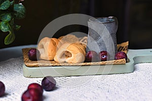 whipped cream tubes with cup and plums on wooven cloth on black background