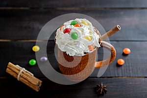 Whipped cream in a wooden mug with a stick of cinnamon and color candies