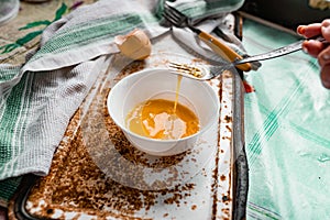 Whipped with a fork and mixed raw egg broken into a white bowl with yolk and protein, next to the shell, fork and towel