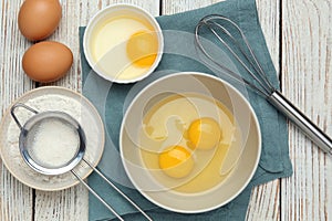 Whisk, eggs in bowl and flour on white wooden table, flat lay