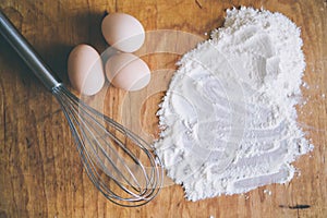 Whisk, eggs and flour on wood board