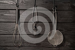 Whisk, masher and strainer hanging against a rustic grey wall in restaurant or home kitchen. Kitchen utensils made of
