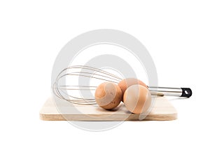 Whisk and three eggs on wood square isolated