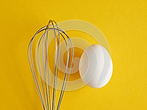 A whisker and a white egg on yellow background. Whisk cooking egg beater mixer whisker