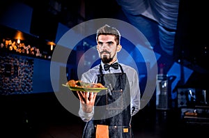 Whiskered waiter offers visitors dish on a black background.