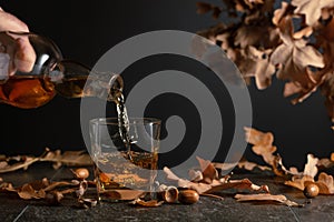 Whiskey on a black table with dried-up oak leaves