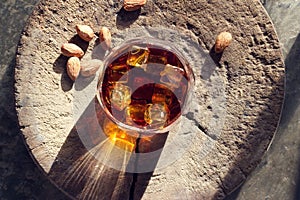 Whiskey bourbon with ices in glass and almonds on old wooden