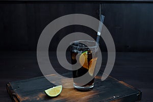 Whiskey with coca cola with ice and slices of fresh lime on a wooden table in the bar