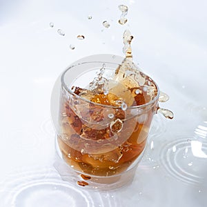 whiskey cocktail with cola and ice in a transparent glass with splashes