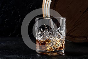 Whiskey in a glass with a barrel. Bourbon whisky and a cask on a dark background