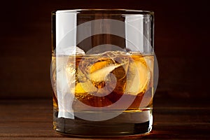 Whiskey in glass with cubes of ice on dark wooden rustic background