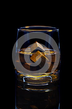 Whiskey in glass with grey whiskey cooling stones on black background