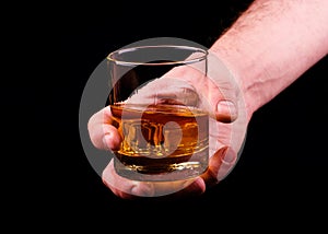 Whiskey glass in a hand of a man on black background, brandy in a glass