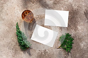 Whiskey glass with ice, blank white business card mockup, coniferous juniper and thuja branches. Male background. Alcohol industry