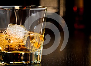 Whiskey glass with ice in front of bottles with space for text