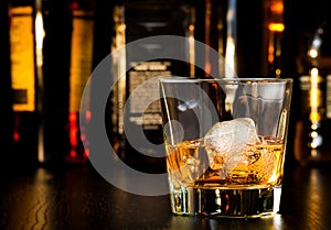 Whiskey glass with ice in front of bottles