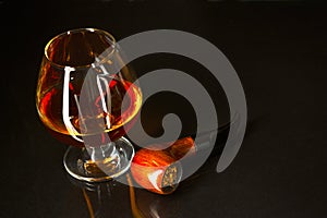 Whiskey glass and smoking pipe on black background