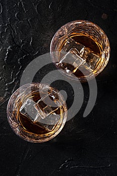 Whiskey in glasses with ice. Bourbon whisky on rocks on a black slate background