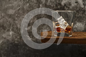 Whiskey with ice or brandy in a glass on a rustic table and gray background. Whiskey with ice in a glass. Whiskey or cognac in a g