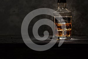 Whiskey with ice or brandy in a glass and a square carafe on an old wooden background. Whiskey with ice in a glass. Whiskey or cog