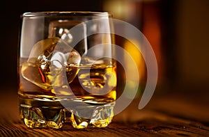 Whiskey with ice cubes. Glass of Whisky and the bottle on wooden table over dark background. Glass of rum alcohol close-up