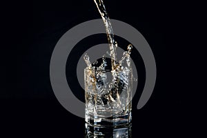Whiskey pouring into glass with ice isolated on black background