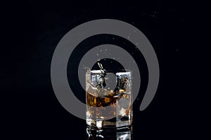 Whiskey splash from the fallen ice cube into glass with beverage isolated on black background