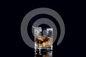 Whiskey splash from the fallen ice cube into glass with beverage isolated on black background