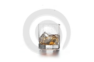 Whiskey splash from the fallen ice cube into glass with beverage on light background