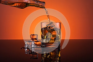 Whisky alcohol pouring into glass with ice drink on orange background
