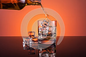 Whisky alcohol pouring into glass with ice drink on orange background