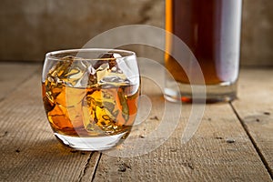 Whisky glass and bottle golden brown ice on wooden surface in saloon bar pub