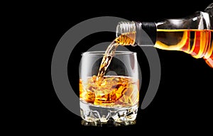 Whisky pouring from the bottle over black. Whiskey on the rocks