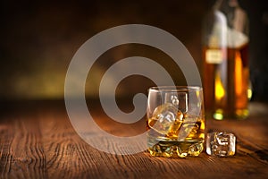 Whisky on the rocks. Glass of whiskey with ice cubes over wooden background