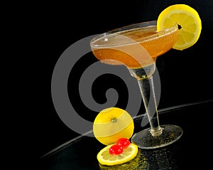 A whisky sour in a coupe glass with a lemon wagon wheel garnish on a round table with dark background. Perspective is tilted.